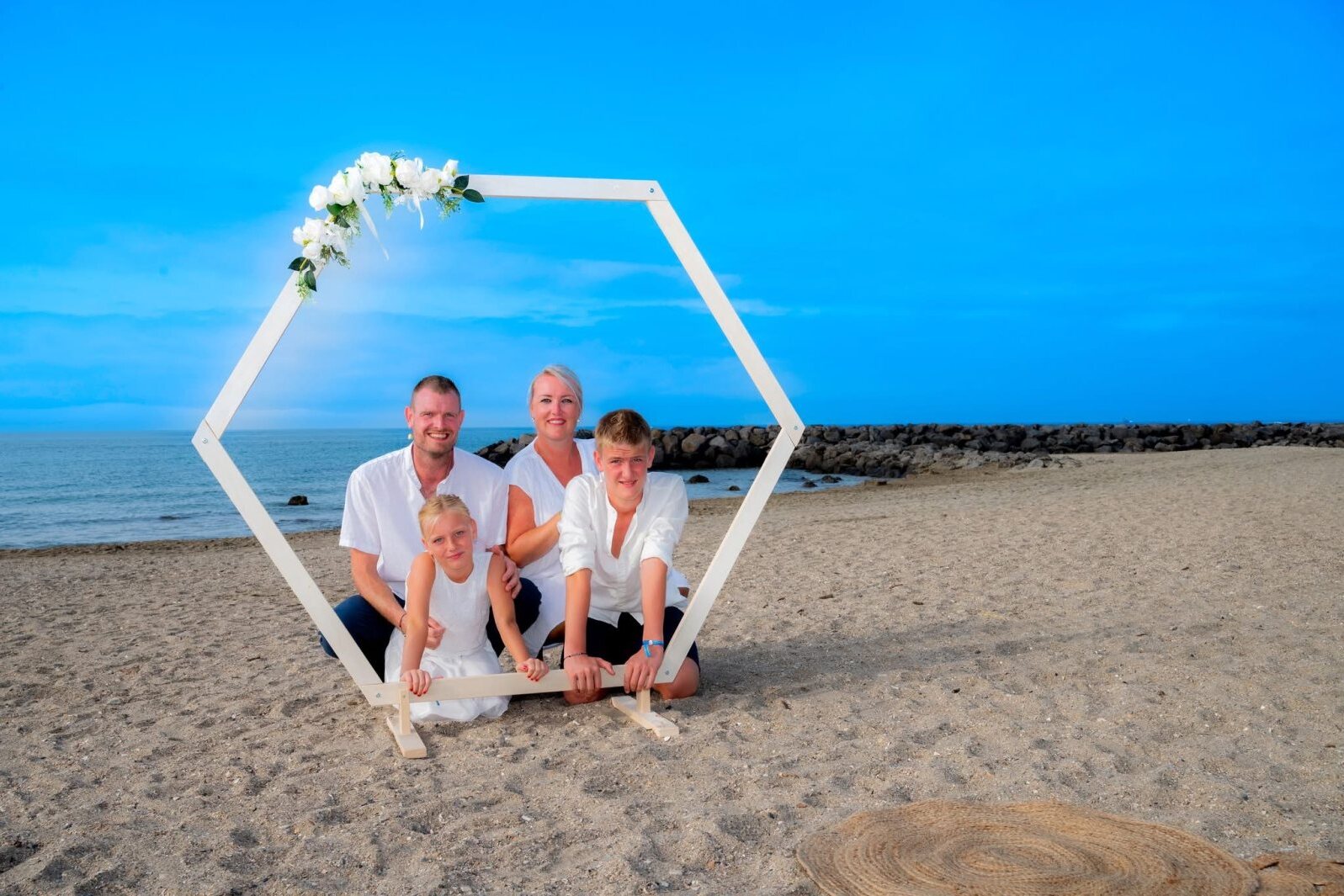 Mariés et leurs enfants sous l'arche à la plage pour leur 10 ans de mariage