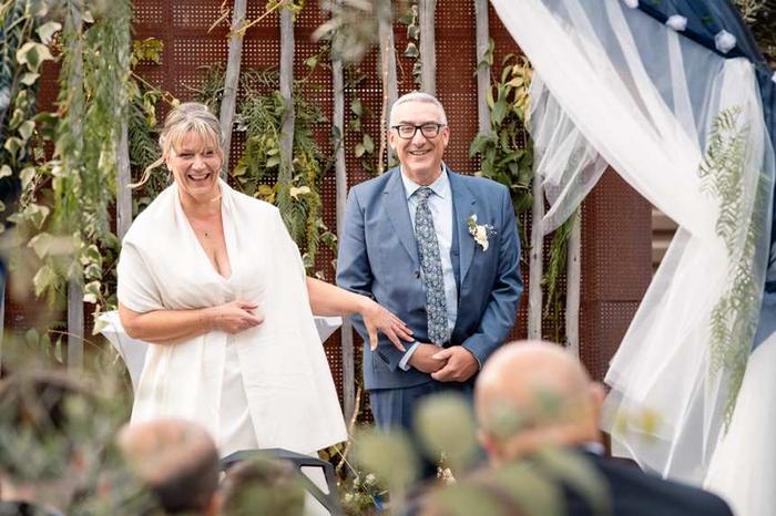 Des mariés rient franchement sous une arche de pampas et de voilage