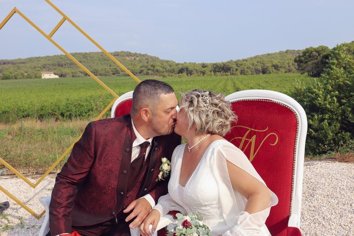 Un couple d’âge mûr s’embrasse dans un fauteuil marqué à ses initiales, les vignes derrière